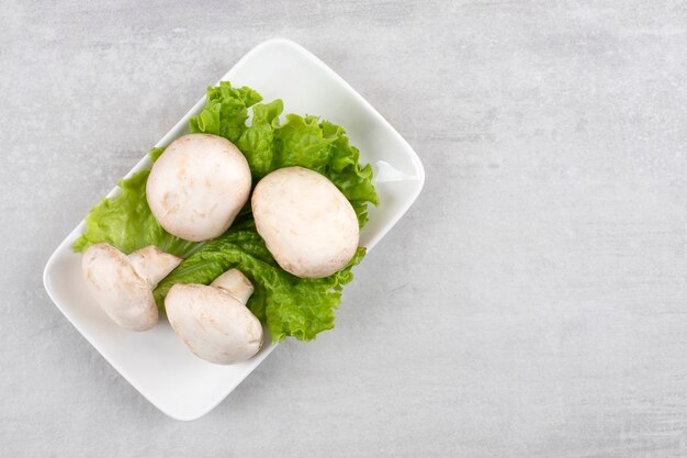 Setas en una hoja de lechuga en un plato, sobre la mesa de mármol.