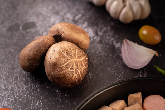 Setas shiitake con ajo y cebolla roja sobre un piso de cemento negro. Enfoque selectivo.