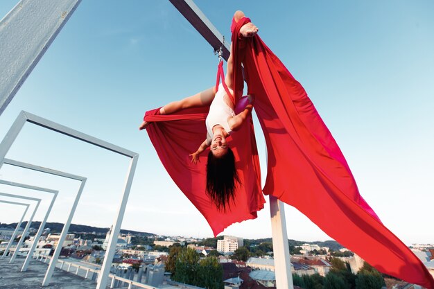 Sexy bailarina realizando danza aérea en el techo al atardecer