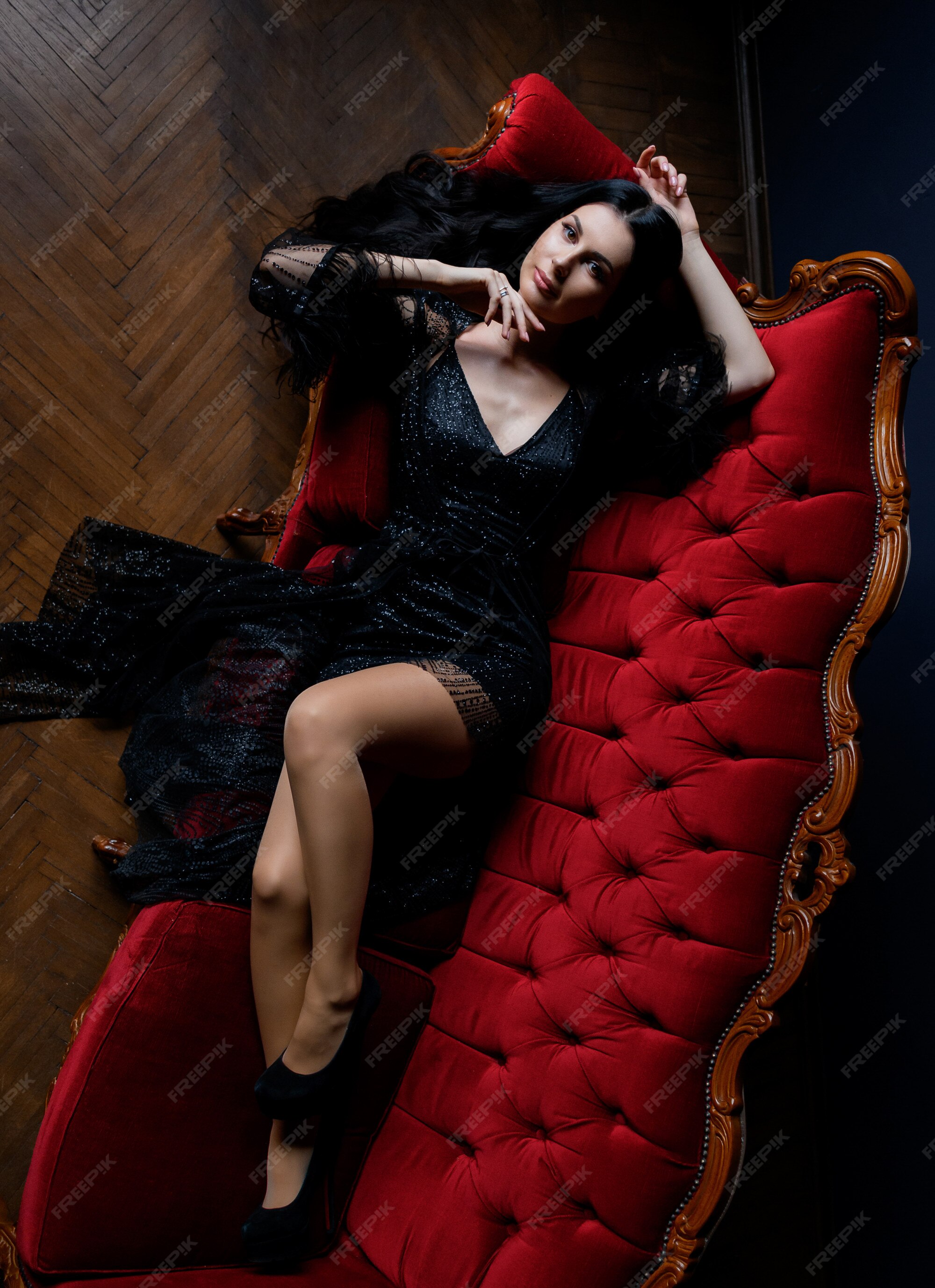 Sexy chica morena de pelo largo está mirando directamente y en el sofá rojo vestido con de encaje negro | Foto Gratis