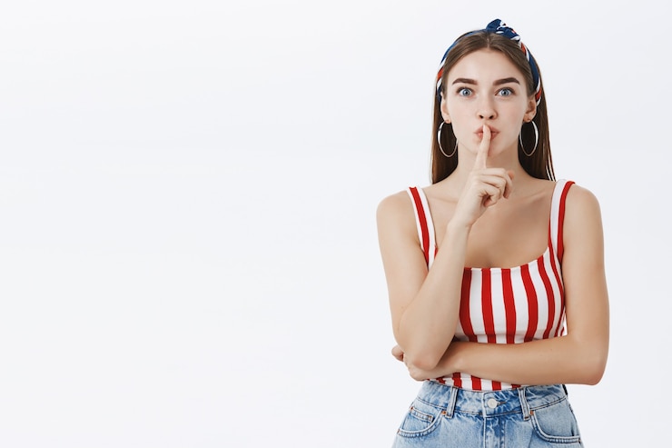 Foto gratuito shh chica va a contar secretos de belleza. encantadora mujer guapa sensual en top a rayas y diadema haciendo gesto de silencio sosteniendo el dedo índice sobre la boca ocultando sorpresa sobre la pared gris