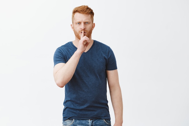 Foto gratuito shh, necesito silencio. retrato de un hombre estricto y guapo de aspecto serio con pelo rojo y cerdas, frunciendo el ceño, haciendo un gesto de silencio con el dedo índice sobre la boca, pidiendo silencio