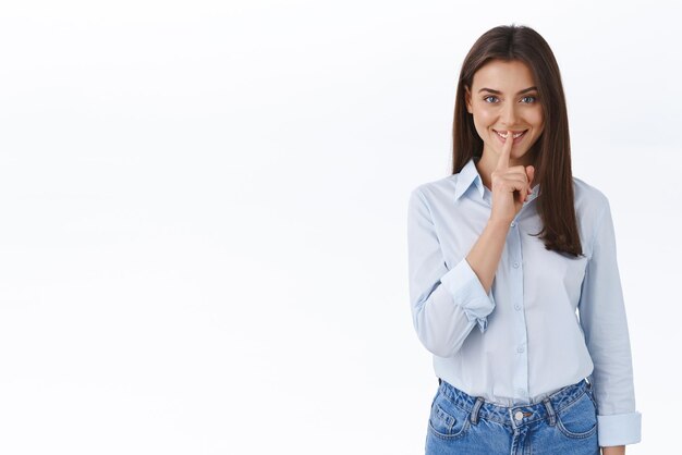 Shh, tengo una sorpresa Misteriosa, feliz y sonriente chica morena con blusa azul, esconde el secreto de los chismes de los compañeros de trabajo y dile que guarde silencio sobre este espectáculo. Gesto de silencio con el dedo índice presionado contra los labios.