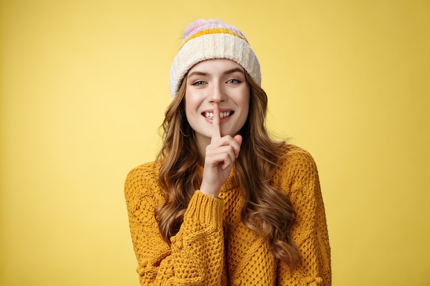 Shush escucha. Retrato atractivo coqueto sonriente desviada linda mujer europea tiene secreto mostrando shh gesto dedo índice presionó los labios compartiendo un rumor interesante, de pie felizmente fondo amarillo