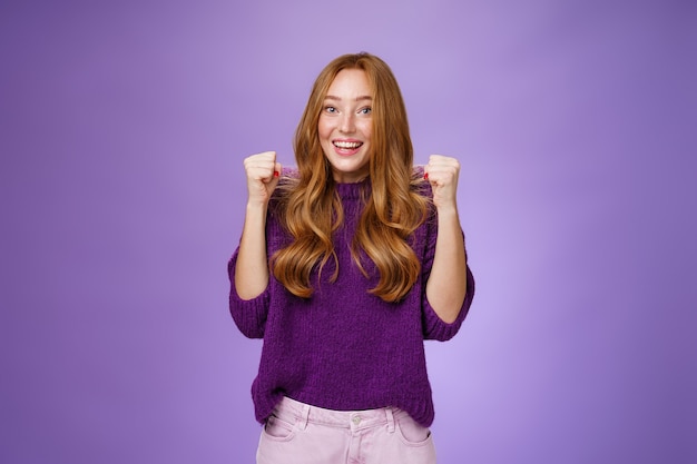 Foto gratuita sí, lo hicimos feliz y alegre jovencita bonita pelirroja con suéter morado sobre fondo violeta ...