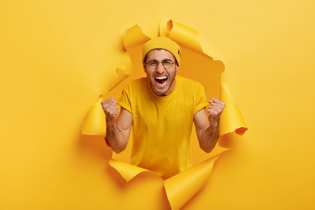 ¡Sí, lo logramos! El hombre emotivo triunfante grita por su equipo favorito, grita de alegría, viste una camiseta y un sombrero amarillo