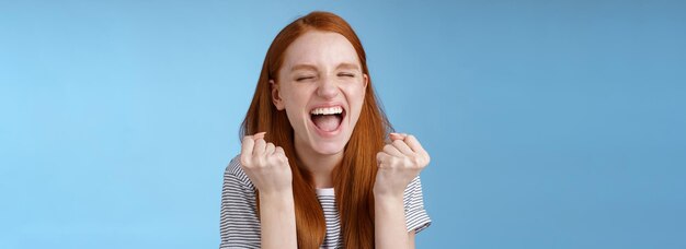 Sí logro meta de toda la vida sonriendo feliz europea pelirroja levantando los puños apretados alegre