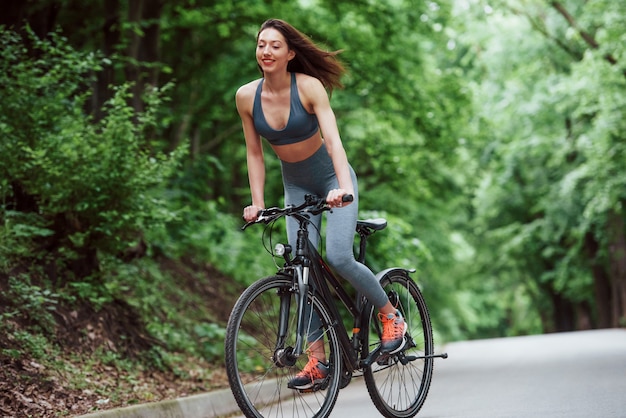 Esto se siente genial. Ciclista femenina en bicicleta por la carretera asfaltada en el bosque durante el día