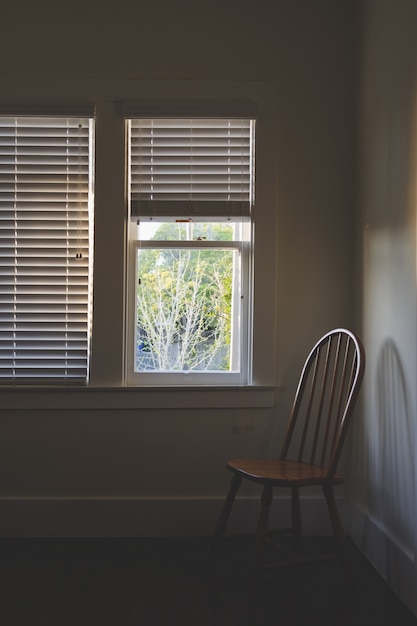 Foto gratuita silla de madera cerca de la ventana con anteojeras