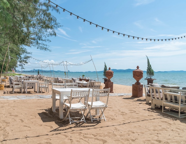sillas blancas y mesa en la playa con una vista del océano azul y cielo claro
