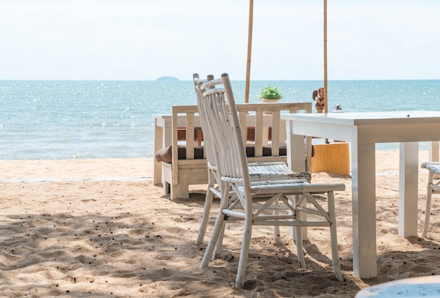 sillas blancas y mesa en la playa con una vista del océano azul y cielo claro