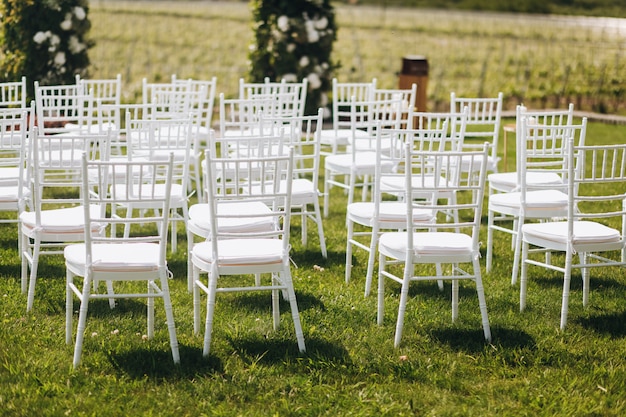 Sillas blancas sobre la hierba delante del arco de la ceremonia de boda