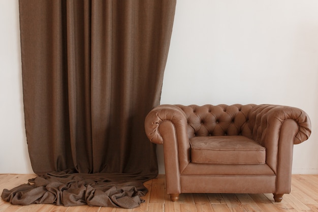 Sillón clásico marrón textil en interior con cortina y piso de madera