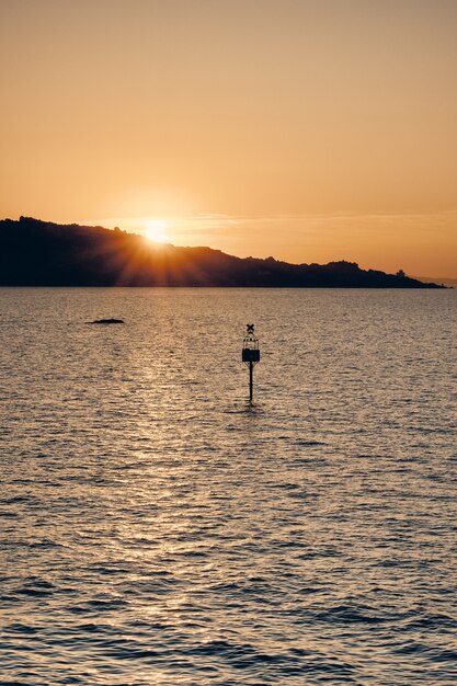 Silueta de un cartel en el agua con el sol brillando detrás de la montaña