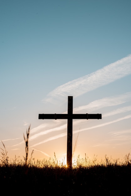 Foto gratuita silueta de cruz de madera en un campo de hierba con un cielo azul en el fondo en un tiro vertical