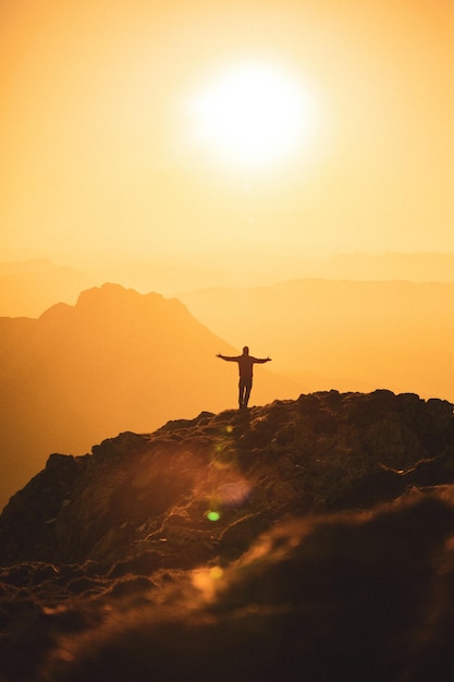 Silueta de un excursionista de espíritu libre en la cima de una montaña al atardecer dorado