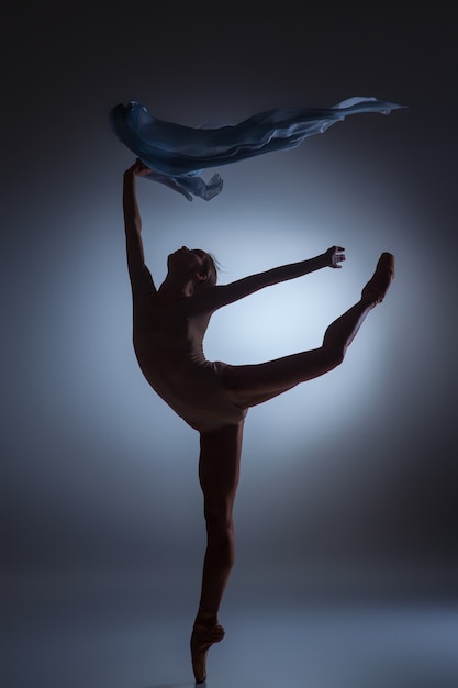 La silueta de la hermosa bailarina bailando con velo sobre fondo azul oscuro