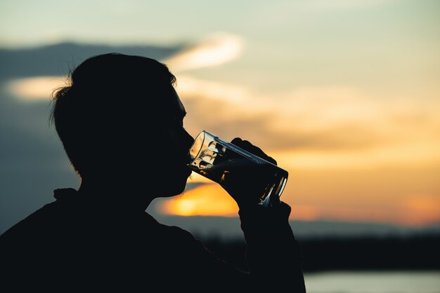 silueta de hombre bebiendo cerveza durante una puesta de sol