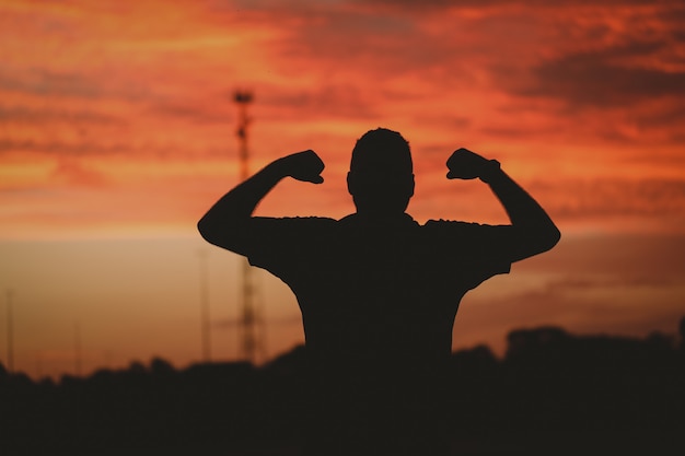 Foto gratuita silueta de un hombre fuerte bajo un cielo nublado durante el atardecer dorado