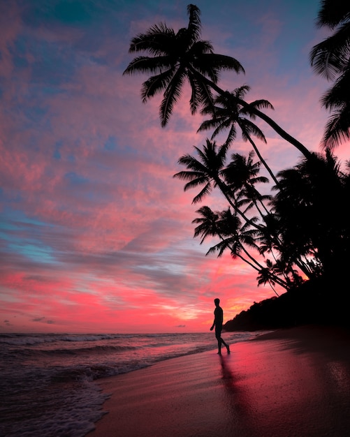 Silueta de un hombre en la playa durante la puesta de sol con increíbles nubes en el cielo rosa