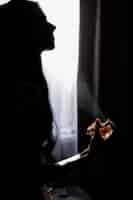 Foto gratuita silueta de joven que está perfumando delante de la ventana en la oscuridad
