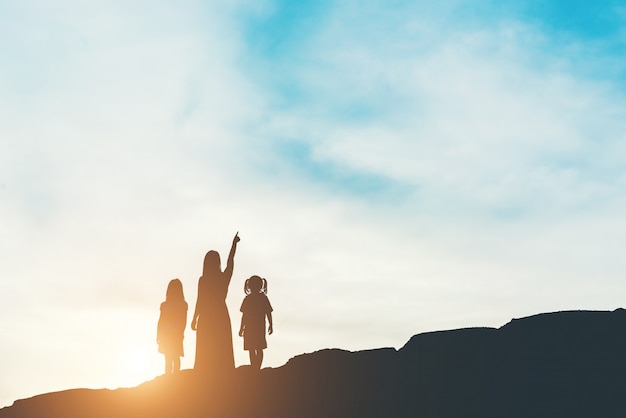 Silueta de la madre con su hija de pie y puesta de sol