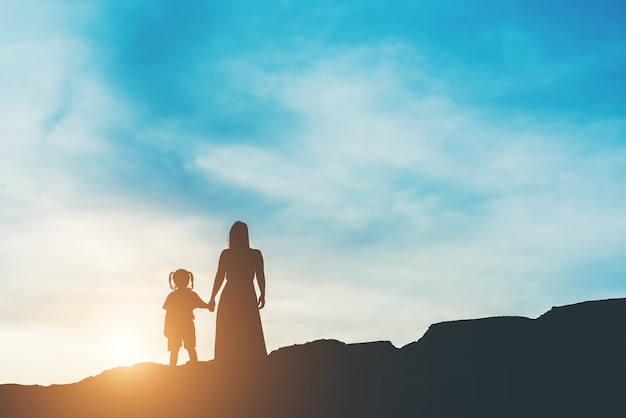 Foto gratuita silueta de la madre con su hija de pie y puesta de sol