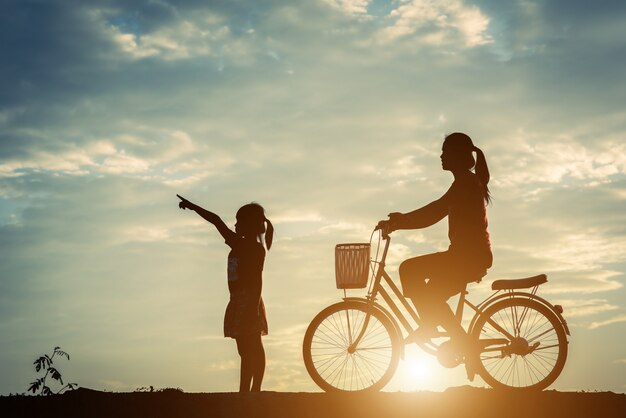 Silueta de madre con su hija y su bicicleta.