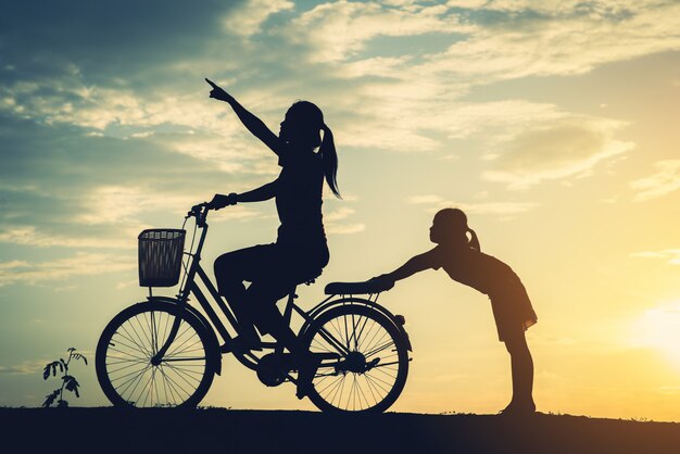 Silueta de madre con su hija y su bicicleta.