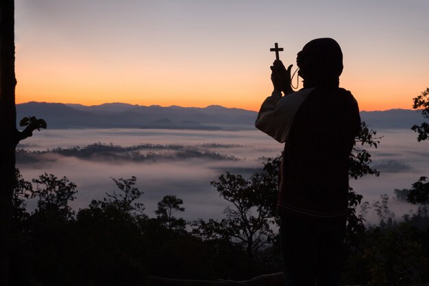 Silueta de mano humana sosteniendo la cruz, el fondo es el amanecer