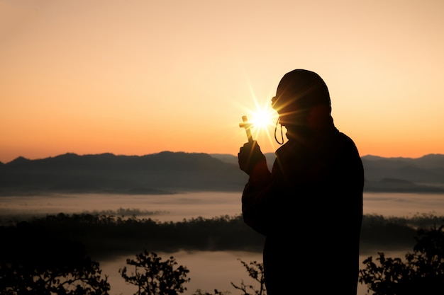 Silueta de mano humana sosteniendo la cruz, el fondo es el amanecer