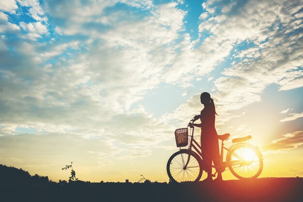 Silueta de mujer con bicicleta y cielo hermoso.