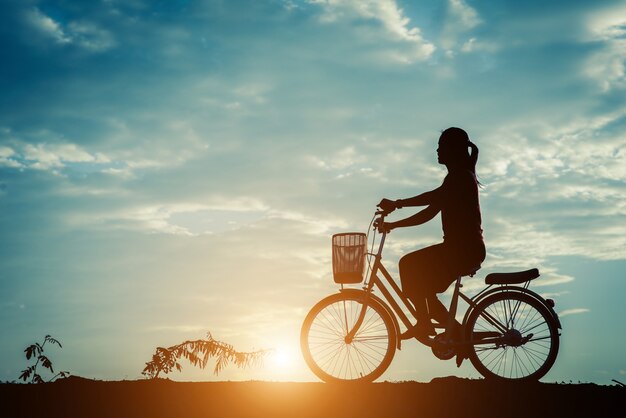Silueta de mujer con bicicleta y cielo hermoso.