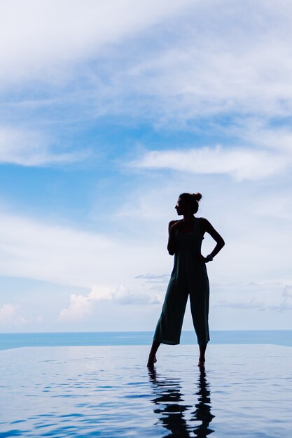 Silueta de una mujer caminando sobre la superficie del agua de la piscina infinita de una costosa villa de lujo rica en una montaña con vista al mar