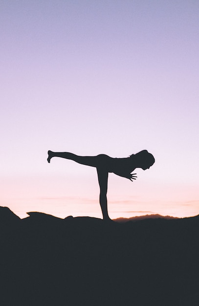 Foto gratuita silueta de una mujer en forma practicando yoga en un acantilado al atardecer