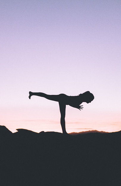 Silueta de una mujer en forma practicando yoga en un acantilado al atardecer