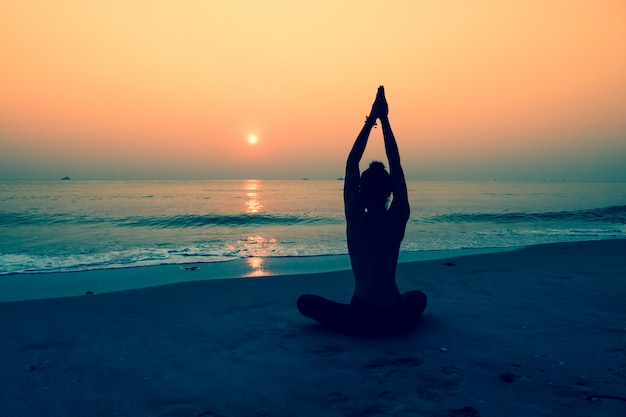 Silueta de mujer haciendo yoga en una playa