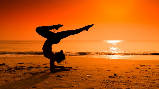 Silueta de mujer haciendo yoga en una playa