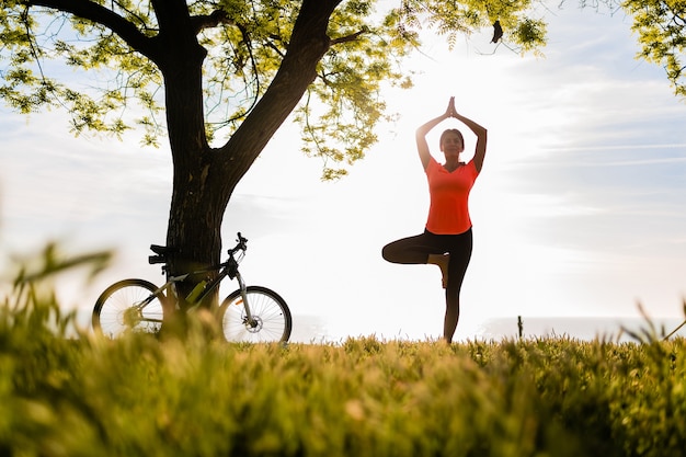 Silueta de mujer hermosa delgada haciendo deporte en la mañana en el parque haciendo yoga