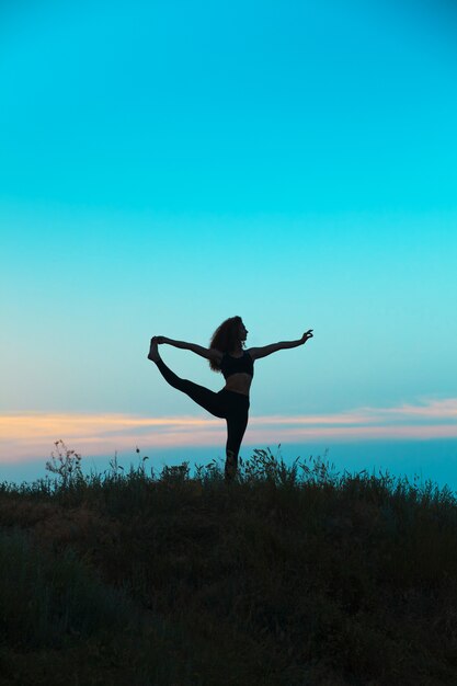 La silueta de la mujer joven está practicando yoga