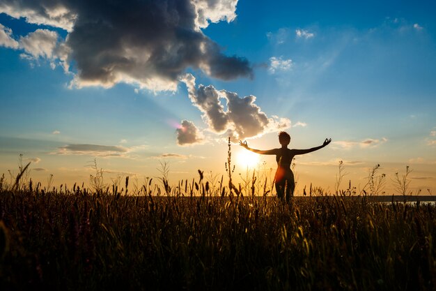 Silueta de niña deportiva practicando yoga en el campo al amanecer.