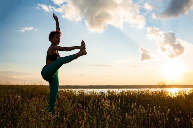 Silueta de niña deportiva practicando yoga en el campo al amanecer.