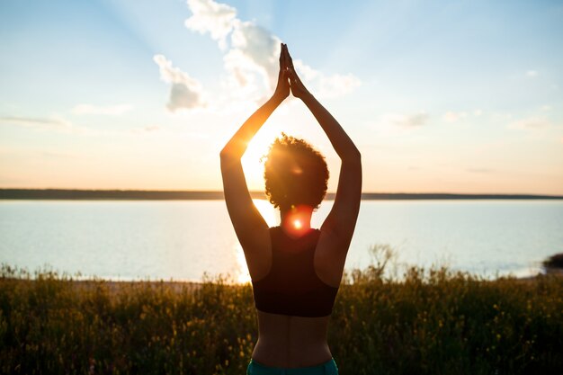 Silueta de niña deportiva practicando yoga en el campo al amanecer.