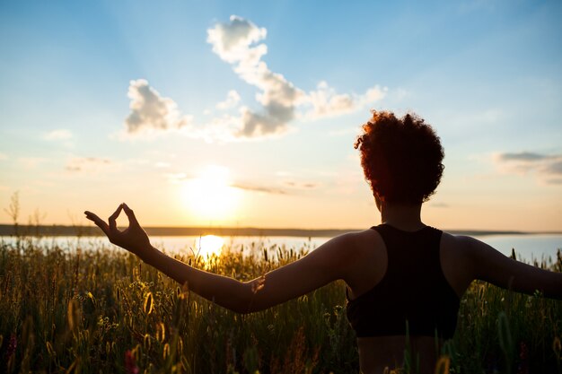 Silueta de niña deportiva practicando yoga en el campo al amanecer.