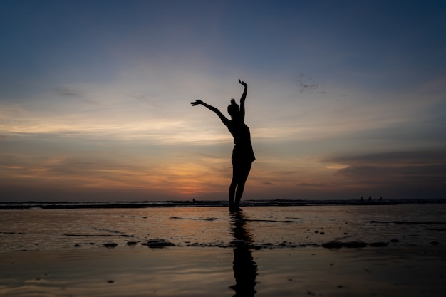 Silueta de una niña de pie en el agua con los brazos levantados gesticulando