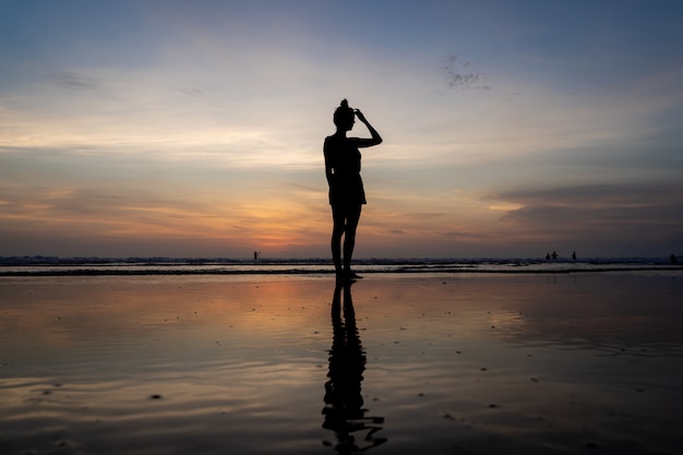 Silueta de una niña de pie en el agua tocando su cabello en una playa