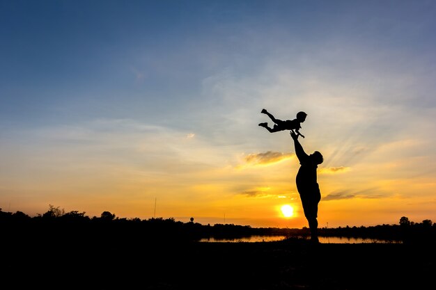 Silueta del padre que lanza al hijo en el cielo. , Padre e hijo en la puesta de sol de fondo