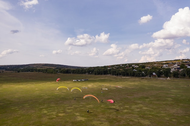 Foto gratuita silueta de parapentes volando sobre un hermoso paisaje verde bajo un cielo azul con nubes.