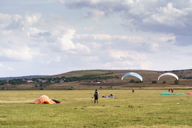 Silueta de parapentes volando sobre un hermoso paisaje verde bajo un cielo azul con nubes.