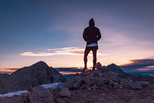 Silueta de persona de pie sobre las rocas mirando la puesta de sol